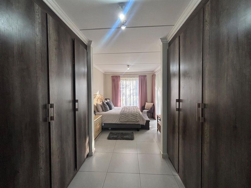 A bedroom featuring extensive built-in cupboards along the hallway entrance, tiled flooring, and natural light flowing from the window.