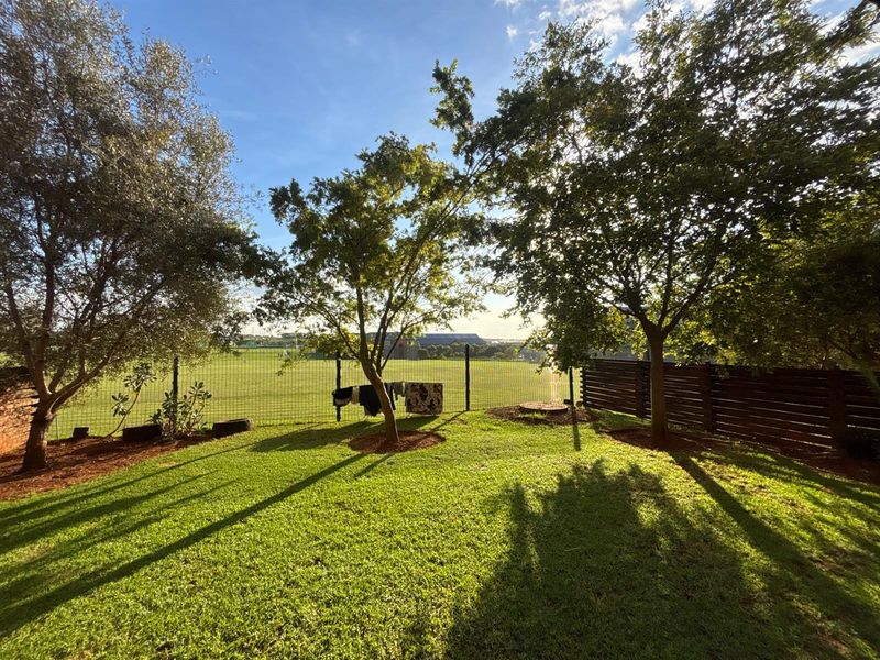 A well-maintained private garden featuring a lush lawn, mature trees, and secure perimeter fencing with views of the surrounding area.