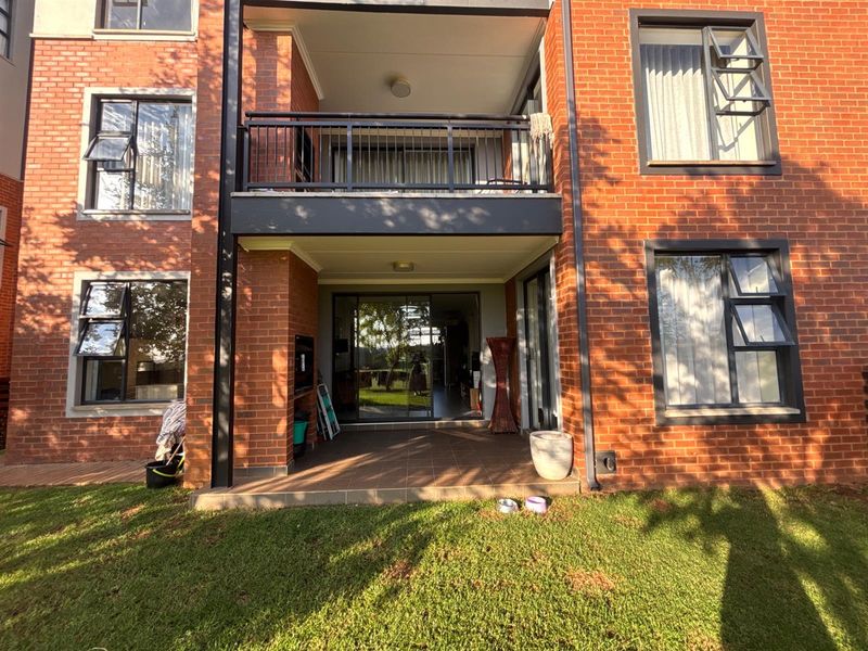 Rear view of a brick apartment building featuring a ground-floor tiled patio, an upper-level balcony with metal railings, and large sliding glass doors.