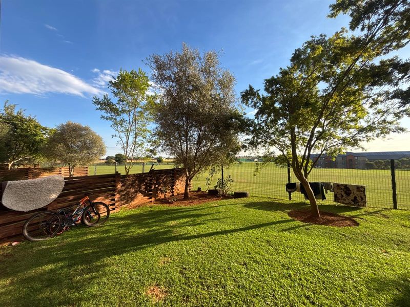 A well-maintained private garden featuring a lush lawn, mature trees, and secure perimeter fencing with timber slat privacy screens.