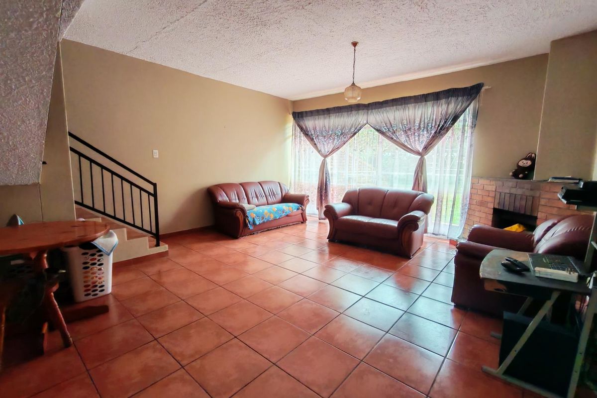 Spacious living room featuring terracotta floor tiles, a built-in brick fireplace, and a staircase with a metal balustrade.
