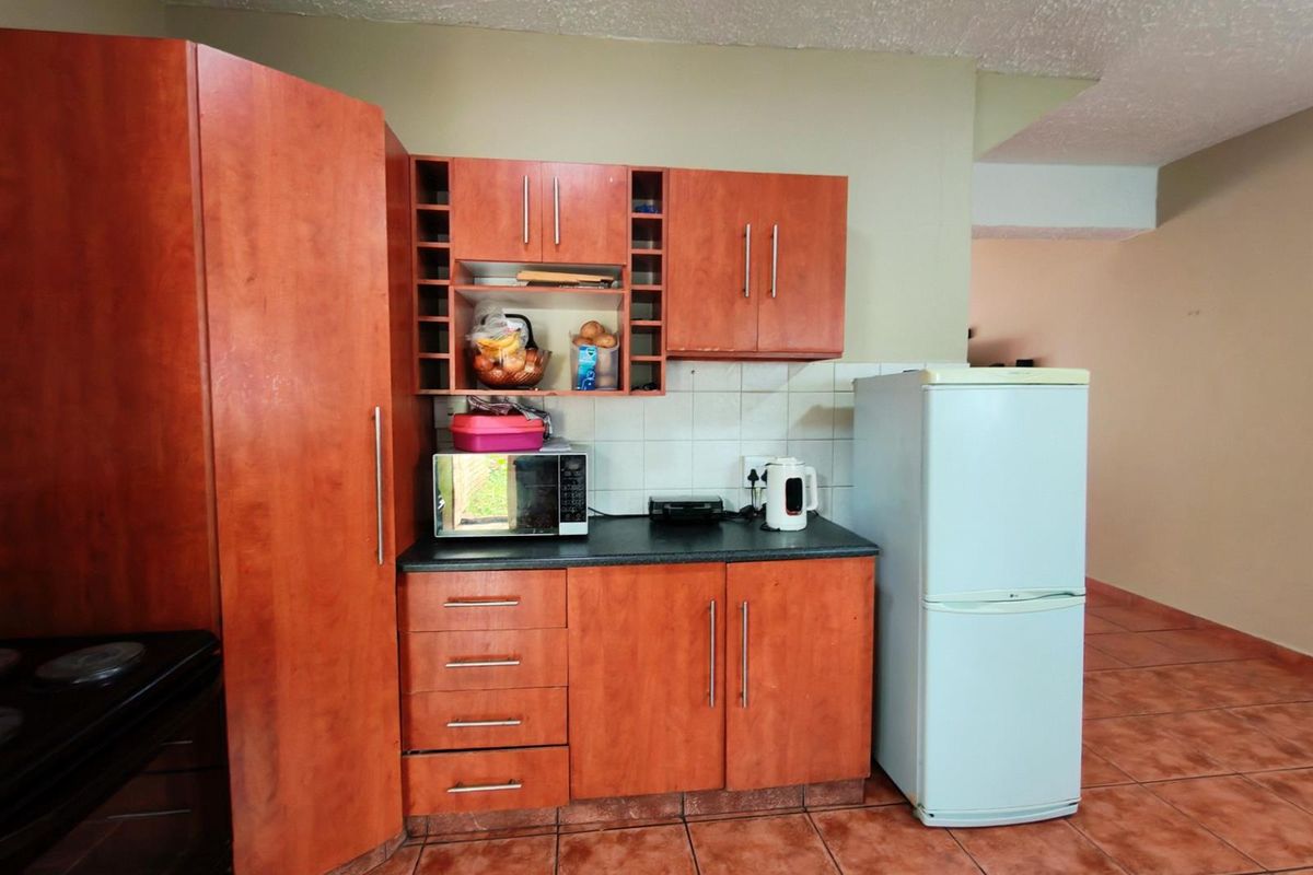 A functional kitchen featuring wood-tone cabinetry, dark countertops, tiled backsplash, and ceramic floor tiles, providing a practical workspace for daily meal preparation.