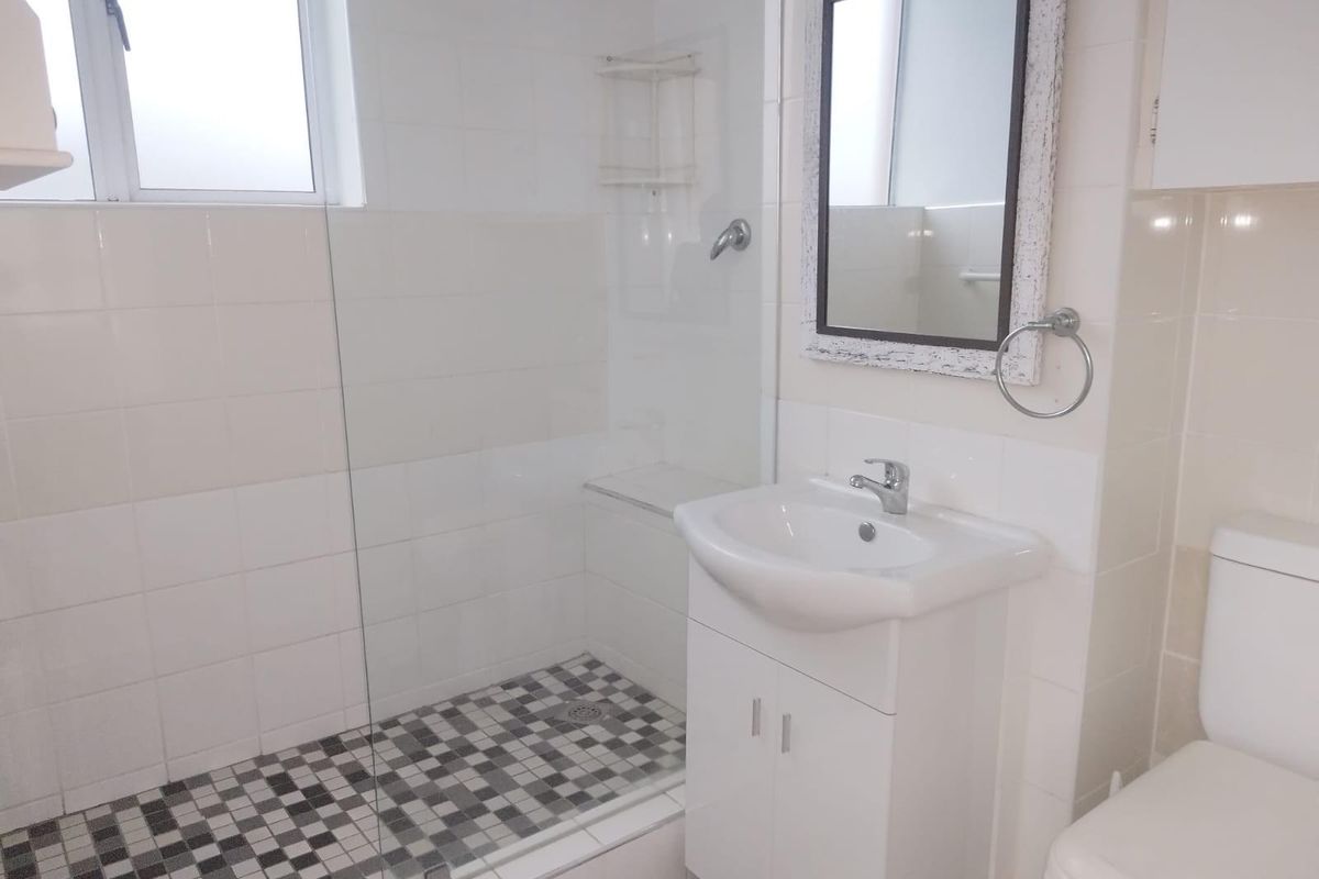 A clean, functional bathroom featuring a walk-in shower with glass screen, vanity cabinet with basin, and a toilet, finished with neutral wall tiles.