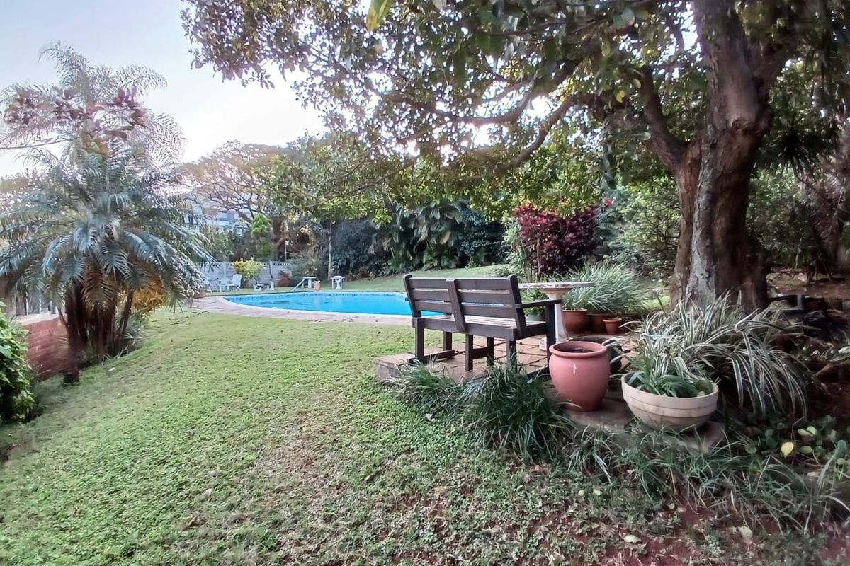 A lush garden setting featuring a swimming pool with paved surround and mature trees, providing a tranquil outdoor space.