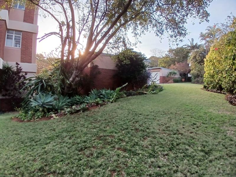 A well-maintained communal garden area featuring mature trees, established landscaping, and brick building facades.