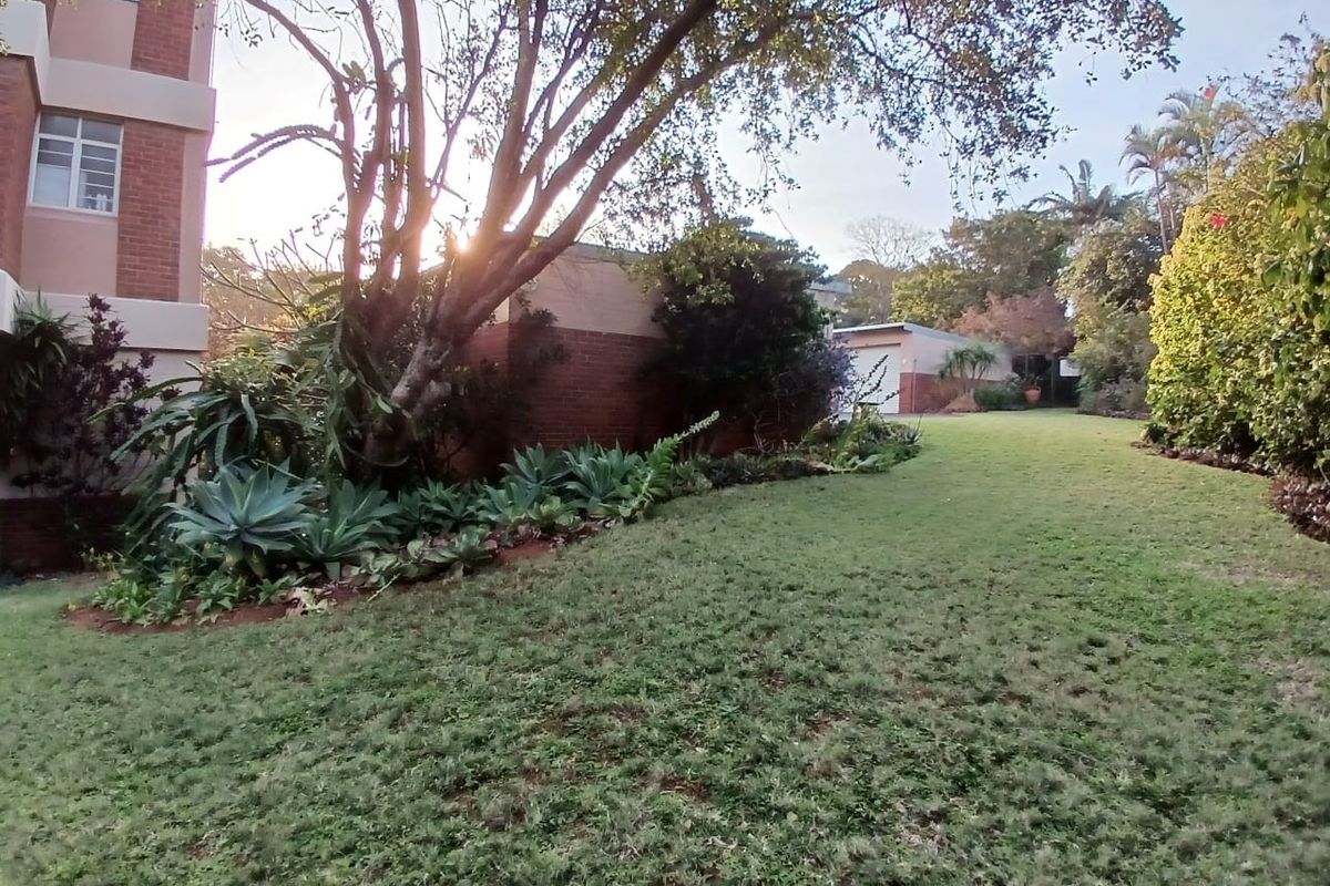 A well-maintained communal garden area featuring mature trees, established landscaping, and brick building facades.