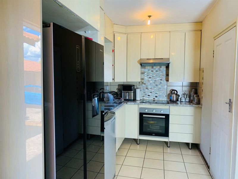 Compact kitchen featuring cream-colored cabinetry, mosaic tile backsplash, built-in oven and hob, and ceramic floor tiles.