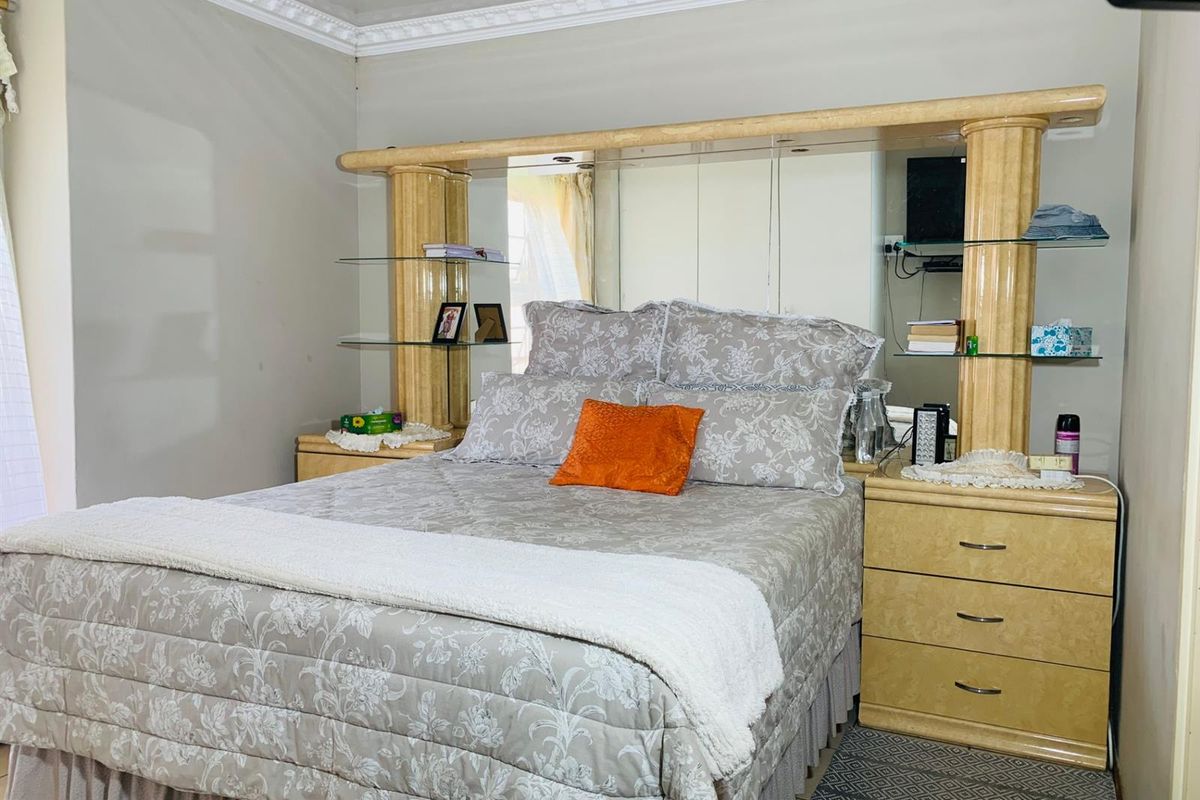 A bedroom featuring a large built-in headboard with integrated mirrored panels, glass shelving, and matching bedside pedestals, complemented by decorative crown molding.