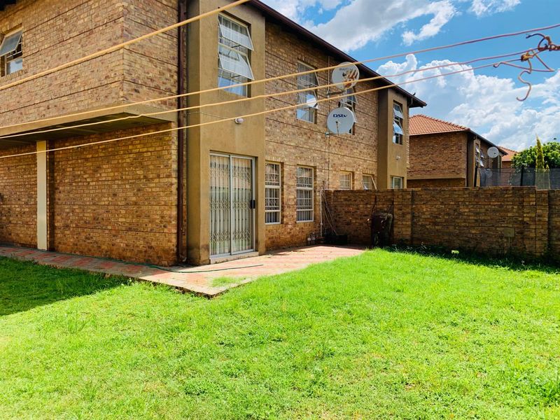 Rear view of a face brick townhouse featuring a paved patio area, private garden space, and secure sliding door access.