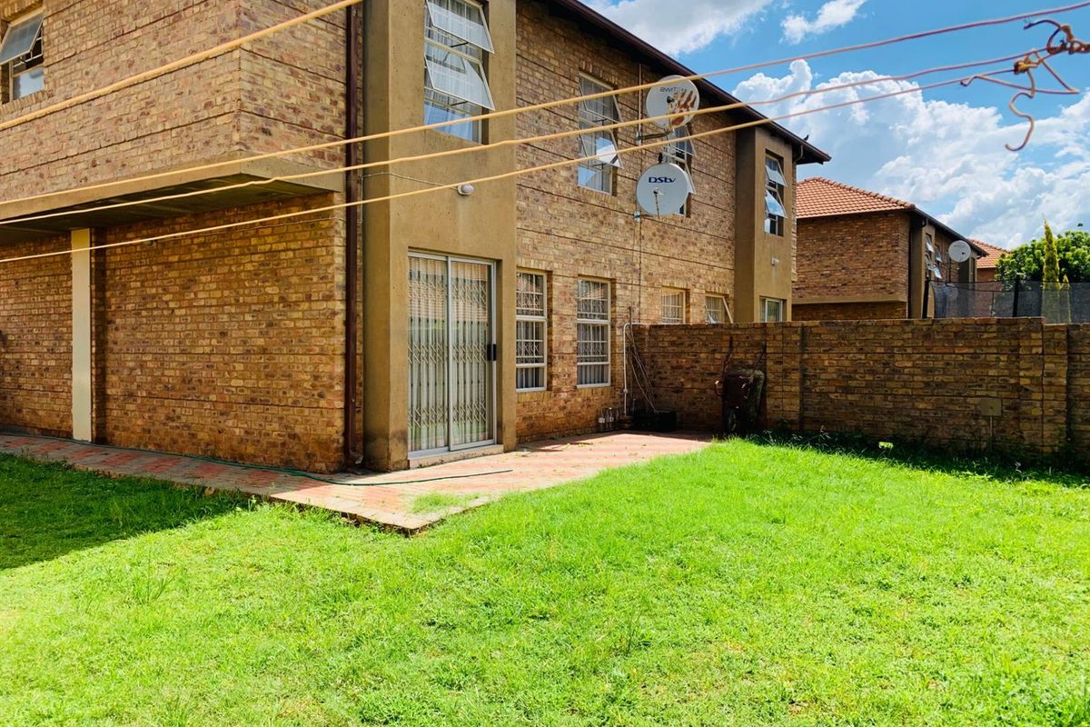 Rear view of a face brick townhouse featuring a paved patio area, private garden space, and secure sliding door access.