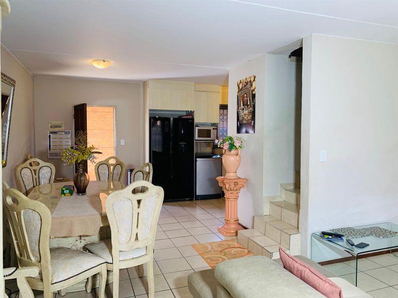 Open-plan living and dining area featuring tiled flooring and an adjacent kitchen with built-in cabinetry and appliances, leading to an internal staircase.