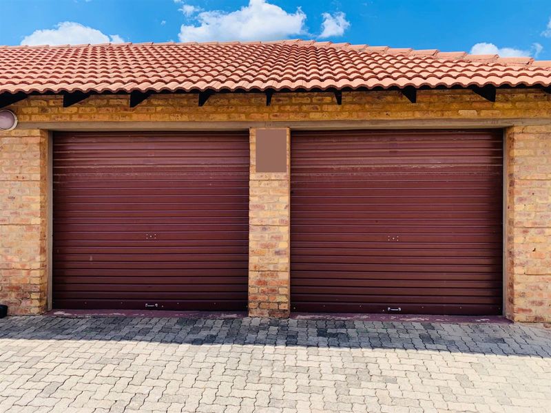 A double garage featuring brown roller doors, a face brick exterior, and a tiled roof, set against a paved driveway.