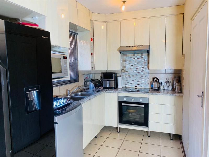Compact kitchen featuring cream cabinetry, mosaic tile backsplash, laminate countertops, and integrated cooking appliances with tiled flooring.