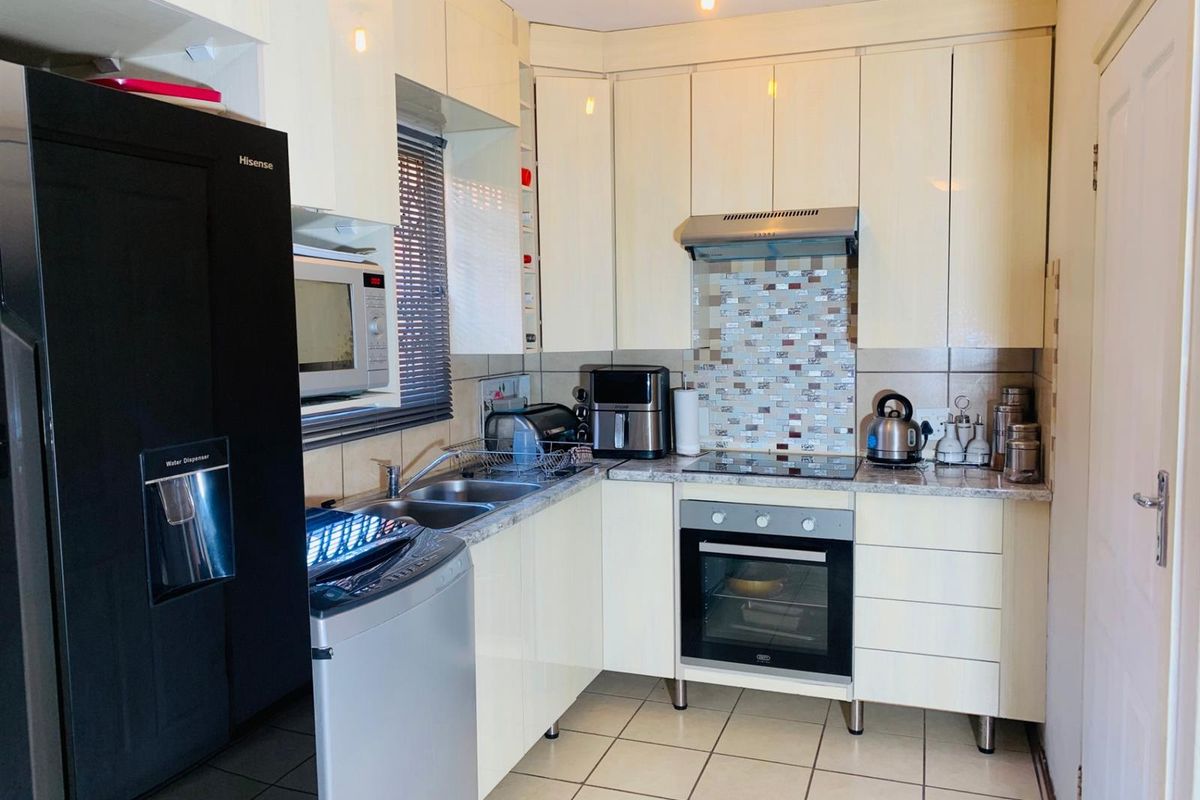 Compact kitchen featuring cream cabinetry, mosaic tile backsplash, laminate countertops, and integrated cooking appliances with tiled flooring.