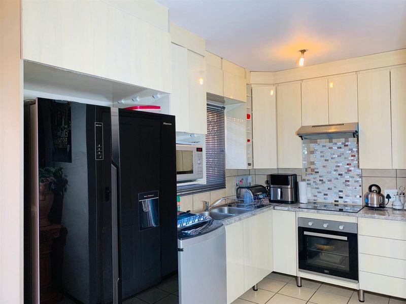A functional kitchen featuring cream-colored cabinetry, mosaic tile backsplash, built-in oven, hob, extractor fan, and tiled flooring.