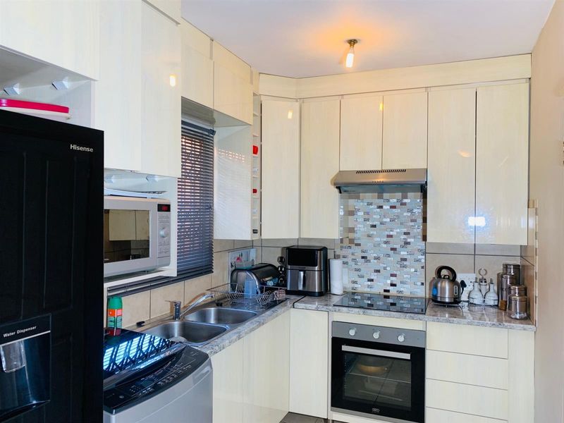A functional kitchen featuring cream-colored cabinetry, a mosaic tile backsplash, integrated oven and hob, and durable laminate countertops.