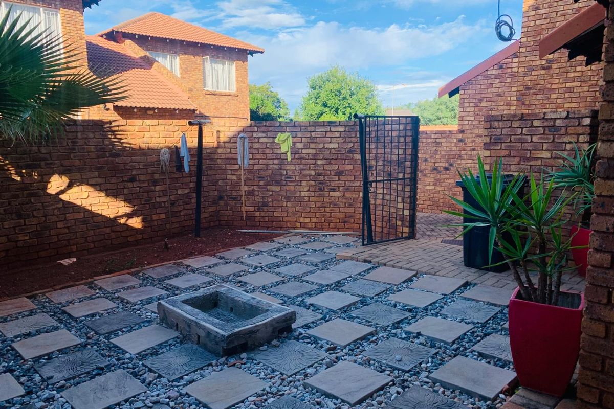 A private rear courtyard featuring brick boundary walls, paved sections with decorative stone inserts, and a built-in concrete basin.