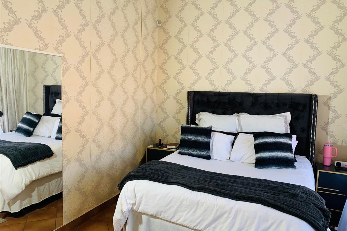 A bedroom featuring patterned wallpaper, tiled flooring, and a large wall-mounted mirror, providing a functional and classic sleeping space.