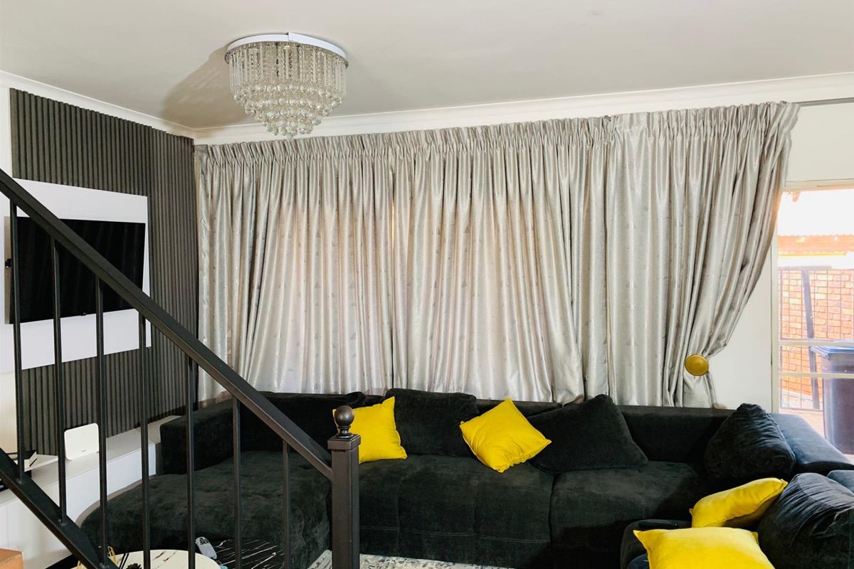 A living room featuring a decorative slatted feature wall, a modern crystal chandelier, and a staircase with a black metal railing.