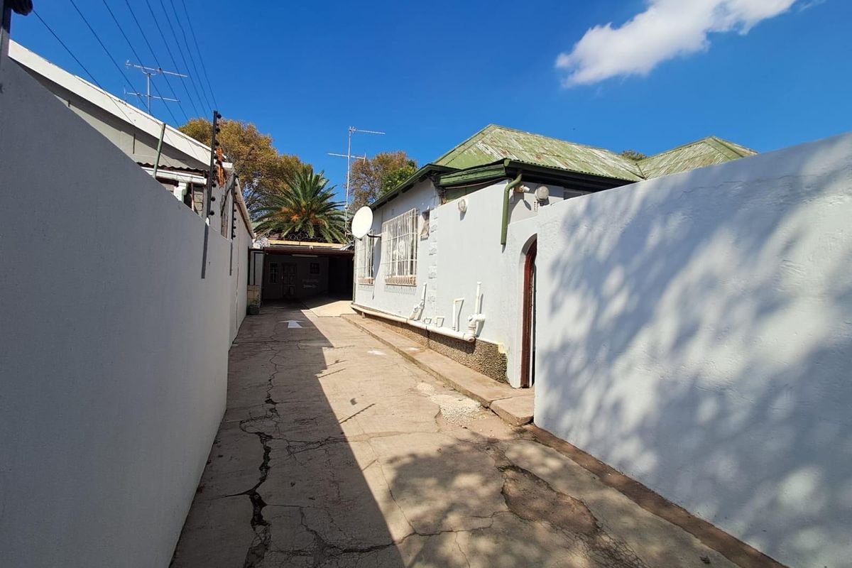 Exterior view of a commercial property side alley featuring a cracked concrete driveway, perimeter boundary walls, and access to the rear building section.