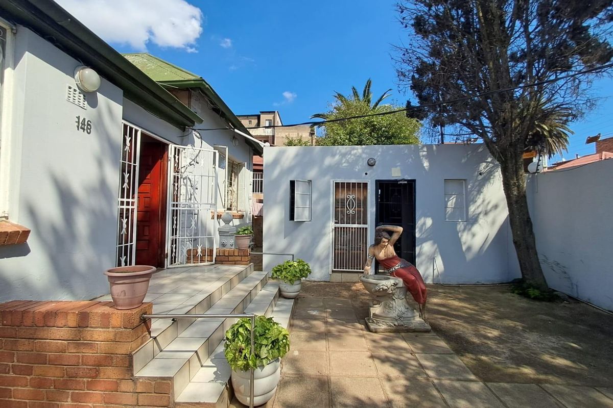 A rear courtyard area featuring tiled steps leading to a building entrance, paved ground, and a secondary structure with security gates.