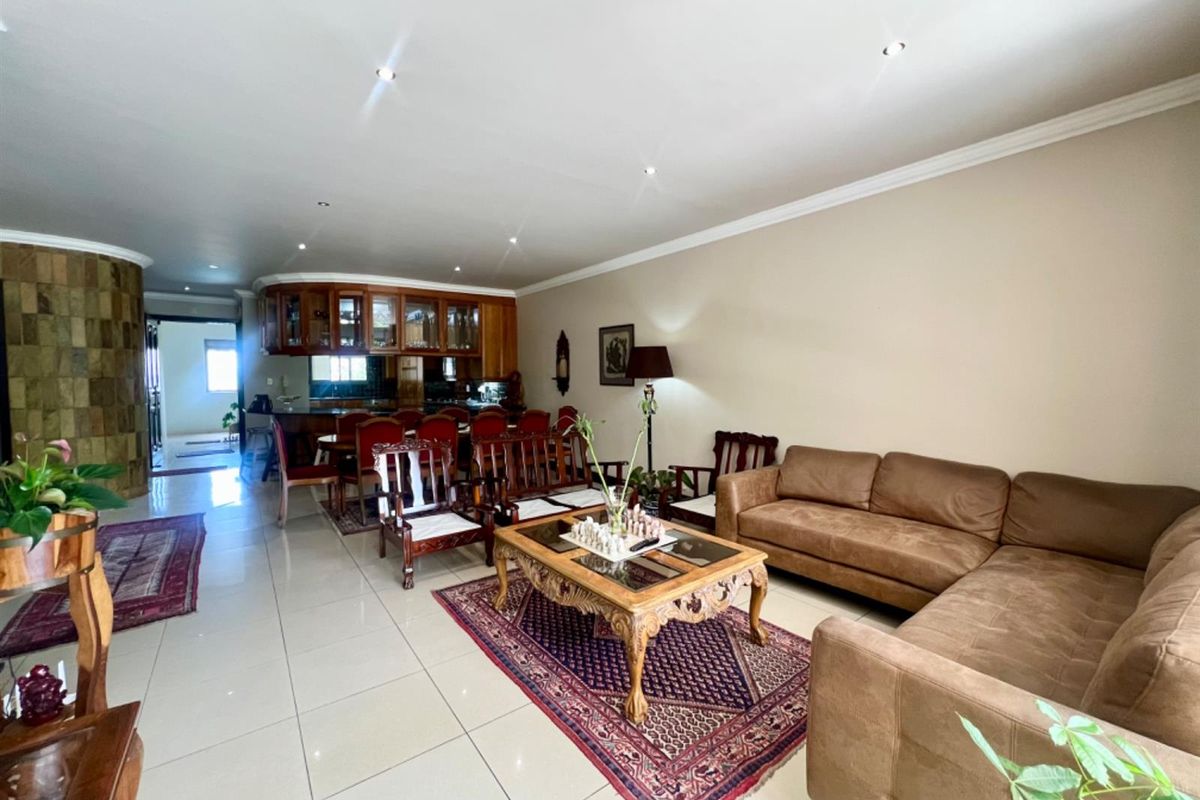 Spacious open-plan living and dining area featuring large format floor tiles, recessed downlighting, and a built-in wooden bar counter.