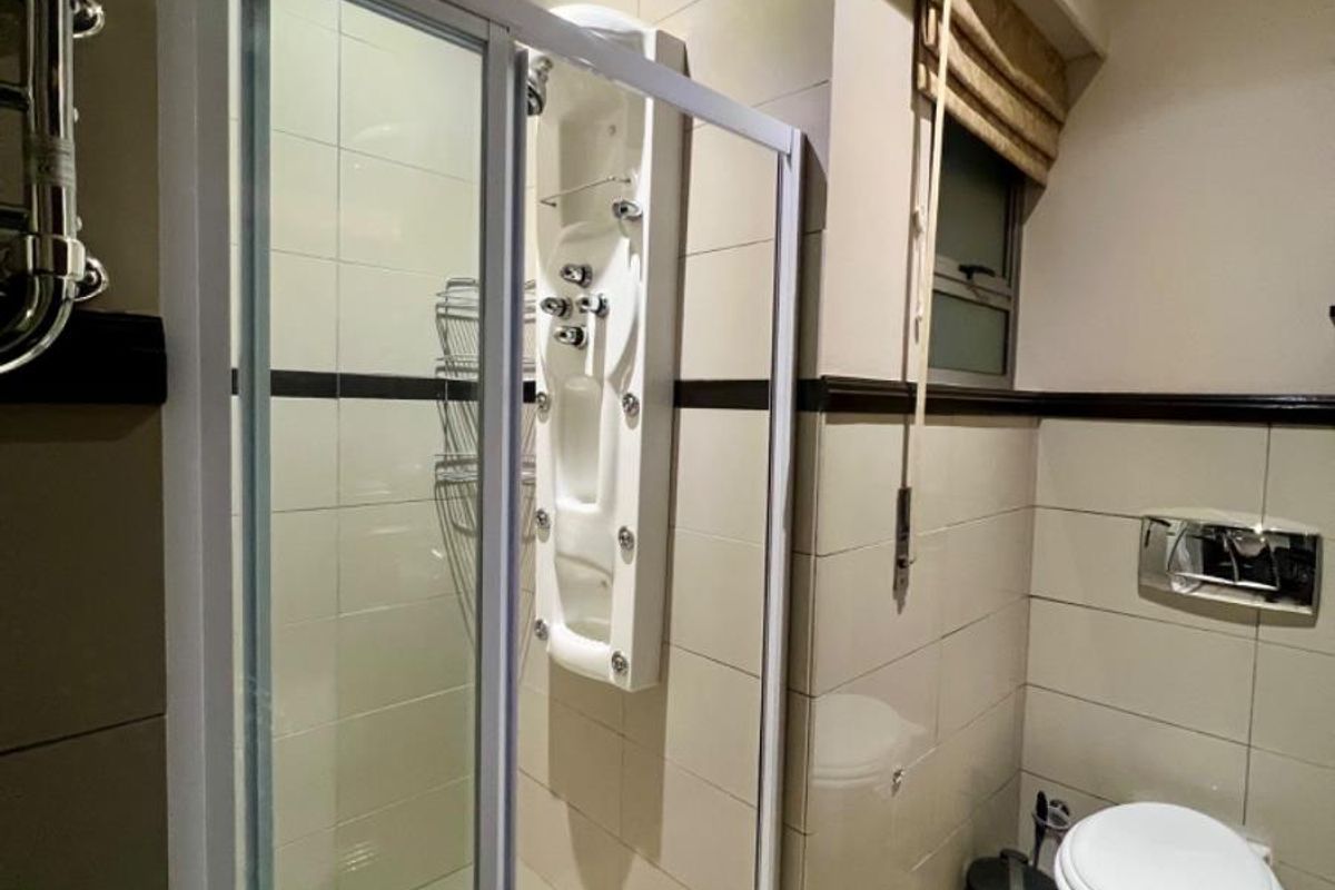 A modern bathroom featuring a glass-enclosed shower with a built-in massage panel, tiled walls, and a wall-mounted toilet.