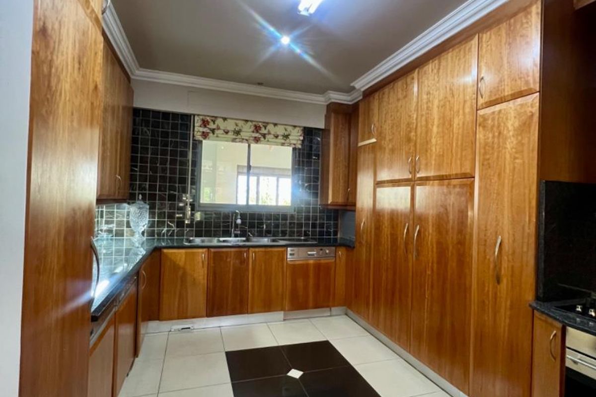 A functional kitchen featuring extensive wooden cabinetry, dark tiled splashbacks, integrated oven, and a contrasting tiled floor layout.