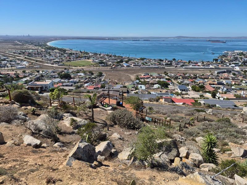 Elevated panoramic view overlooking the coastal town, bay, and harbour, featuring a wooden viewing deck in the foreground.