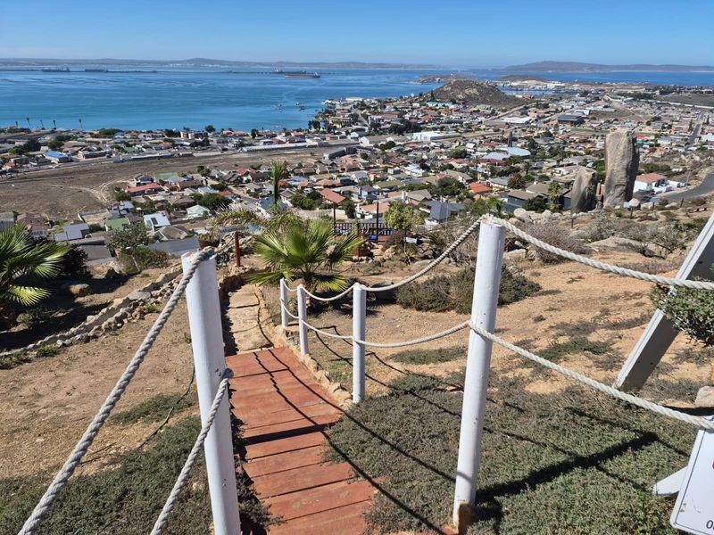 Elevated view overlooking the coastal town and bay, featuring a rustic wooden staircase with rope railings leading down the hillside.