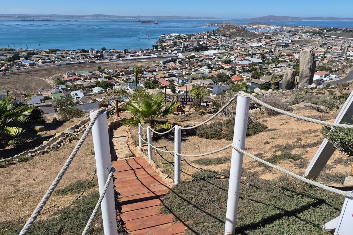 Elevated view overlooking the coastal town and bay, featuring a rustic wooden staircase with rope railings leading down the hillside.