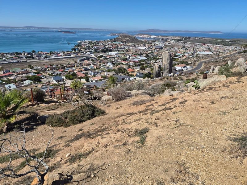 Elevated panoramic view overlooking the coastal town, harbor, and surrounding landscape, showcasing the natural topography and residential setting of the area.