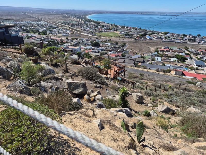 Elevated panoramic view overlooking the coastal town, bay, and surrounding landscape from a rocky hillside vantage point.