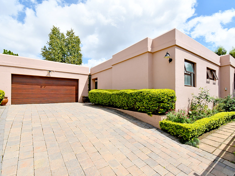 Front elevation of the property featuring a paved driveway, double garage, and well-maintained garden hedging.
