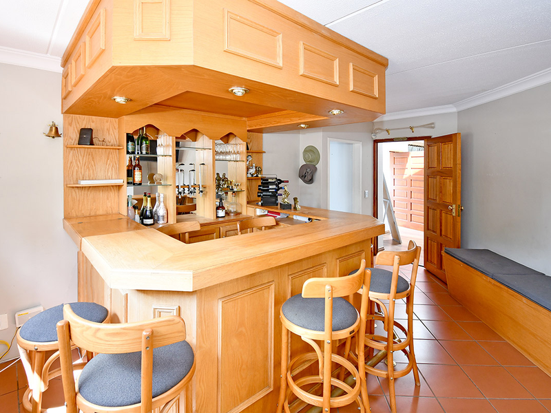 A dedicated bar area featuring a substantial built-in wooden counter, overhead canopy with integrated lighting, mirrored shelving, and built-in bench seating.
