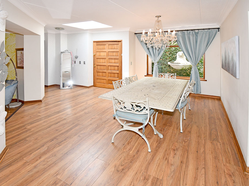 Spacious dining area featuring timber-look laminate flooring, a large skylight for natural light, and a classic crystal chandelier.