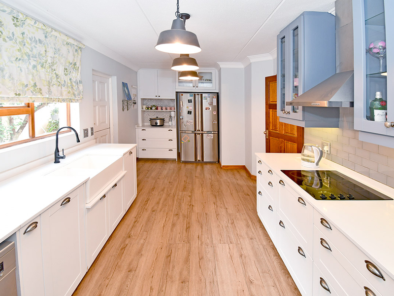 Modern kitchen featuring white shaker cabinetry, farmhouse sink, induction cooktop, subway tile backsplash, and wood-look laminate flooring with ample storage space.