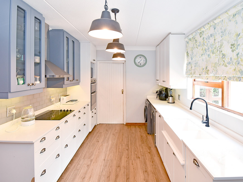 A modern, well-appointed kitchen featuring blue and white cabinetry, quartz countertops, an apron sink, and high-quality integrated appliances with stylish pendant lighting.