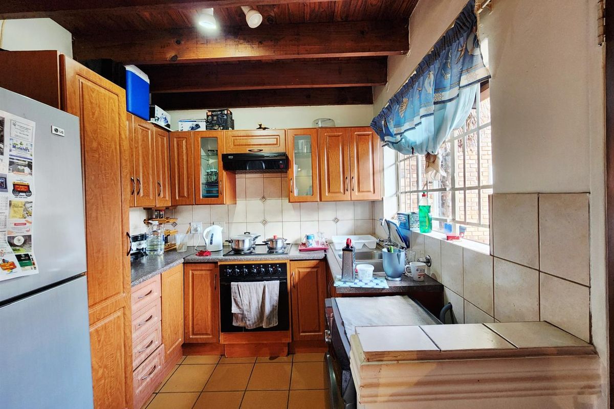 A functional kitchen featuring wooden cabinetry, tiled countertops, a built-in oven with extractor fan, and exposed timber ceiling beams.