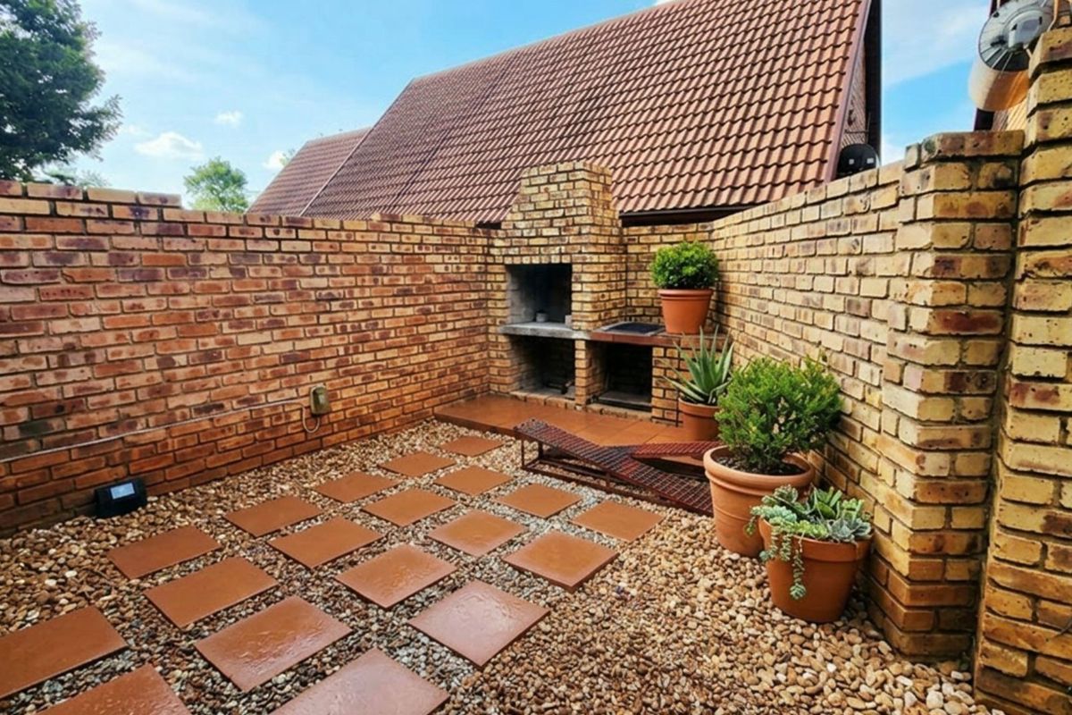 A private rear courtyard featuring a built-in brick braai, paved stepping stones, and decorative gravel, enclosed by high face-brick boundary walls.