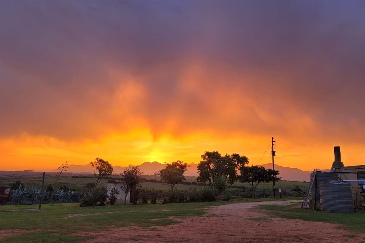 A scenic sunset view over the farm landscape, featuring a water tank and outdoor chimney structure in the foreground.