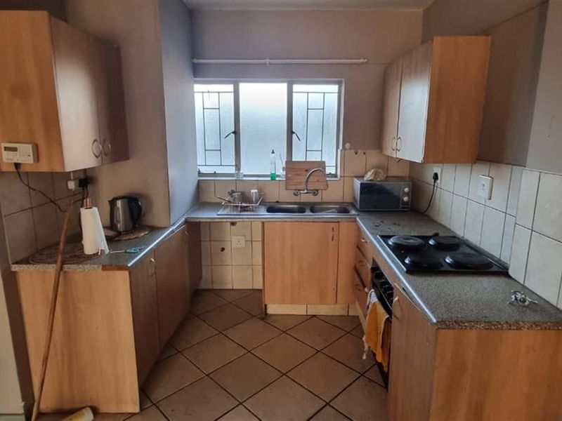 A functional kitchen featuring laminate cabinetry, stone-look countertops, an electric hob, and tiled flooring, offering a practical layout with potential for modern updates.