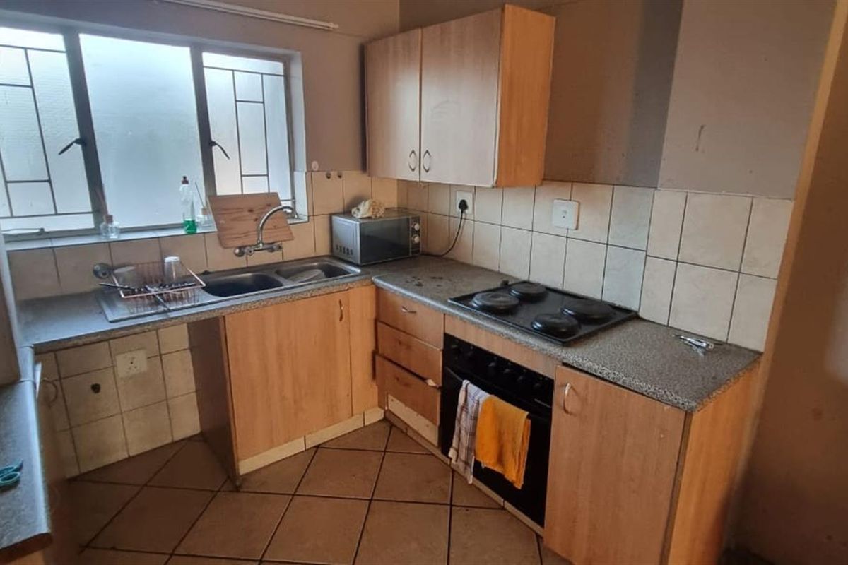 A functional kitchen featuring built-in cabinetry, laminate countertops, a stainless steel sink, and an integrated electric hob and oven with tiled backsplash.