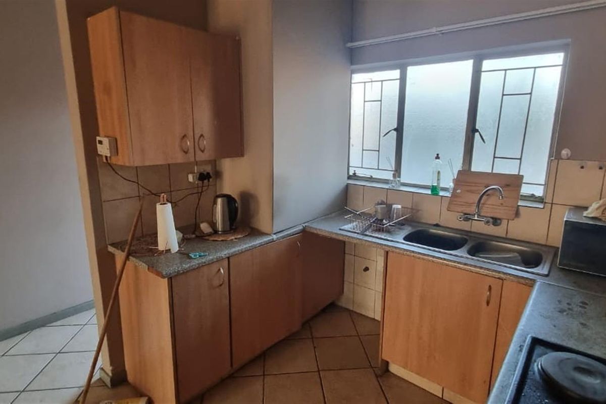 A functional kitchen featuring laminate cabinetry, a double bowl stainless steel sink, tiled splashback, and built-in hob, offering a practical layout for daily use.