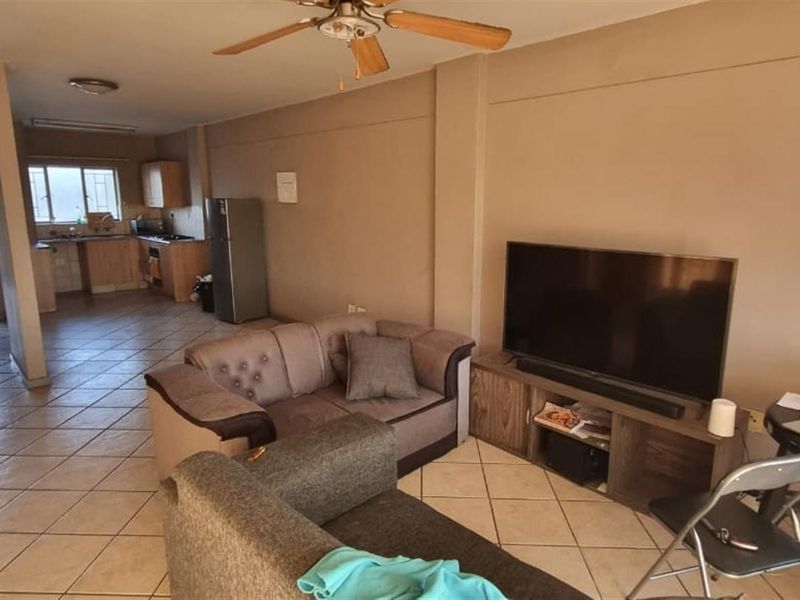 Open-plan living area featuring tiled flooring, a ceiling fan, and an adjoining kitchen with built-in cabinetry and appliances.
