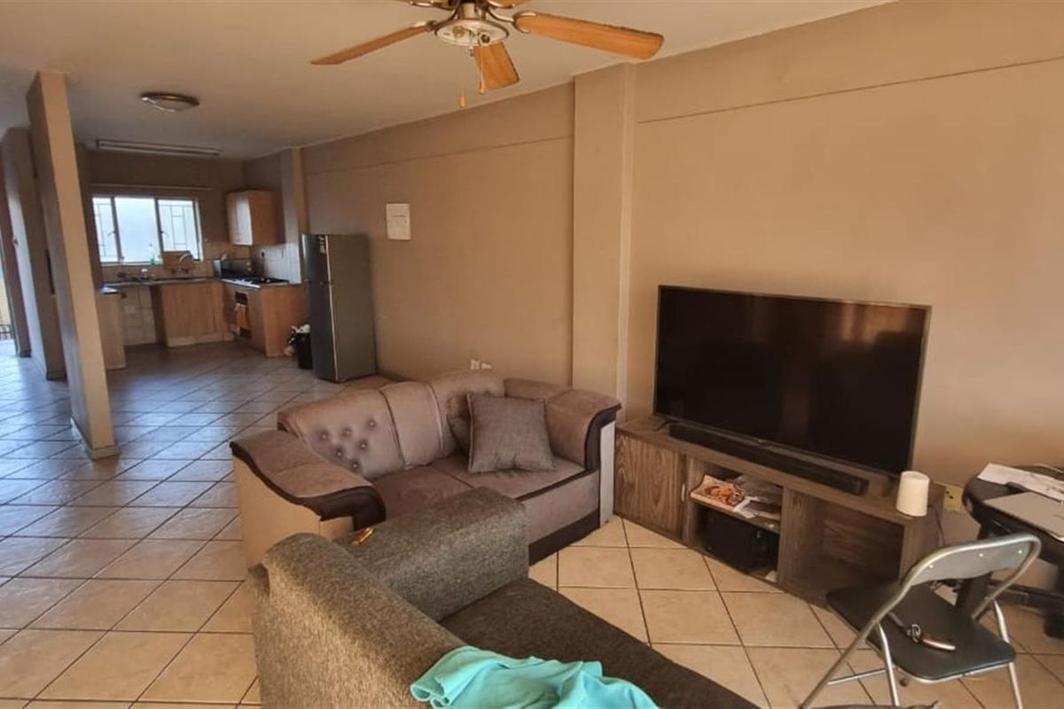 Open-plan living area featuring tiled flooring, a ceiling fan, and an adjoining kitchen with built-in cabinetry and appliances.