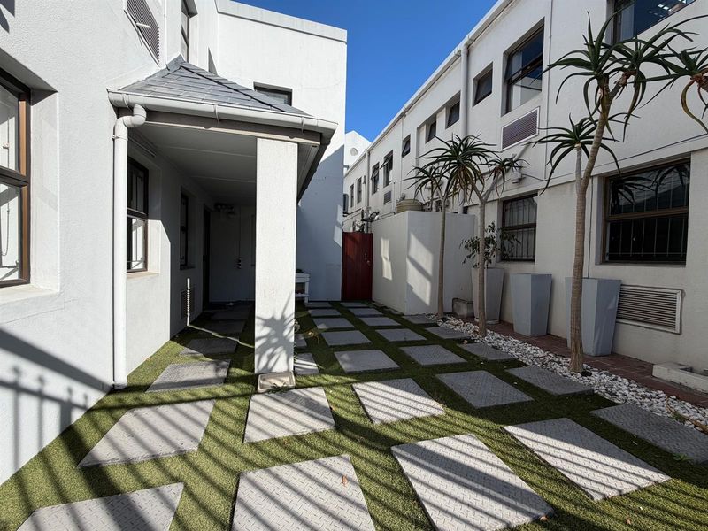 A well-maintained rear courtyard area featuring a paved walkway, artificial turf, and a covered patio section between office building wings.