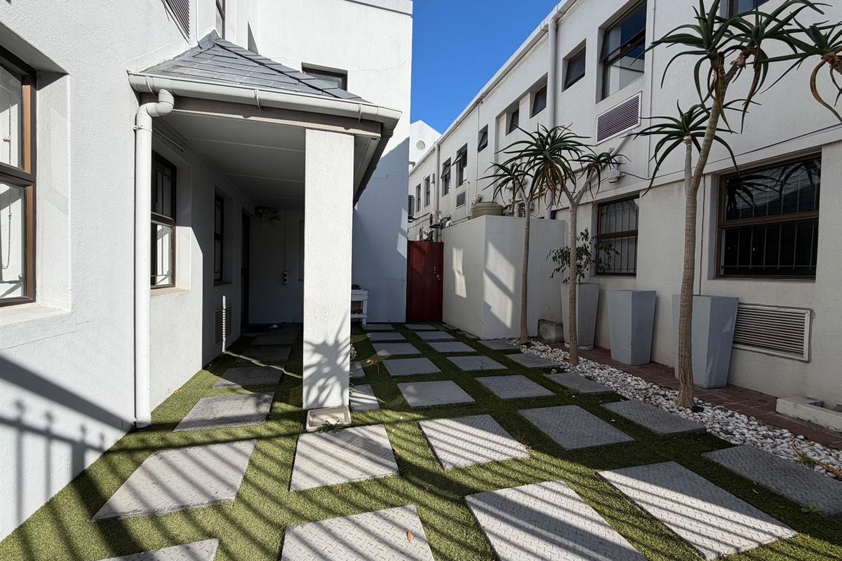 A well-maintained rear courtyard area featuring a paved walkway, artificial turf, and a covered patio section between office building wings.