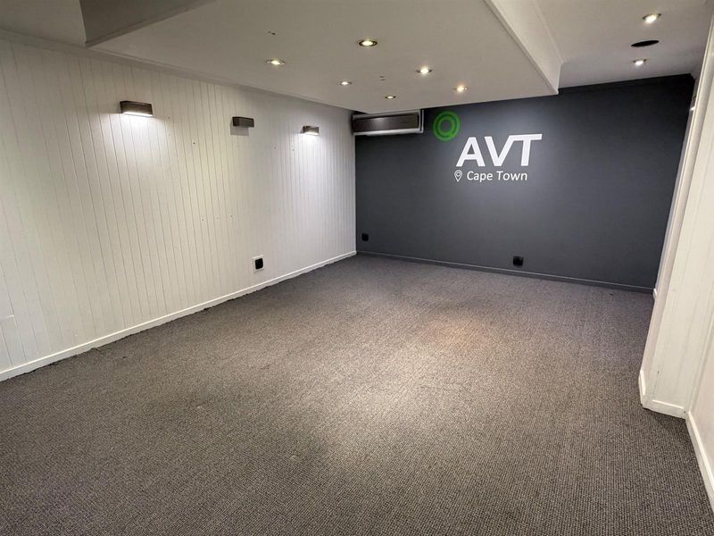 A clean, empty office space featuring recessed lighting, wall-mounted accent lights, air conditioning, and neutral carpeting, suitable for a professional workspace.