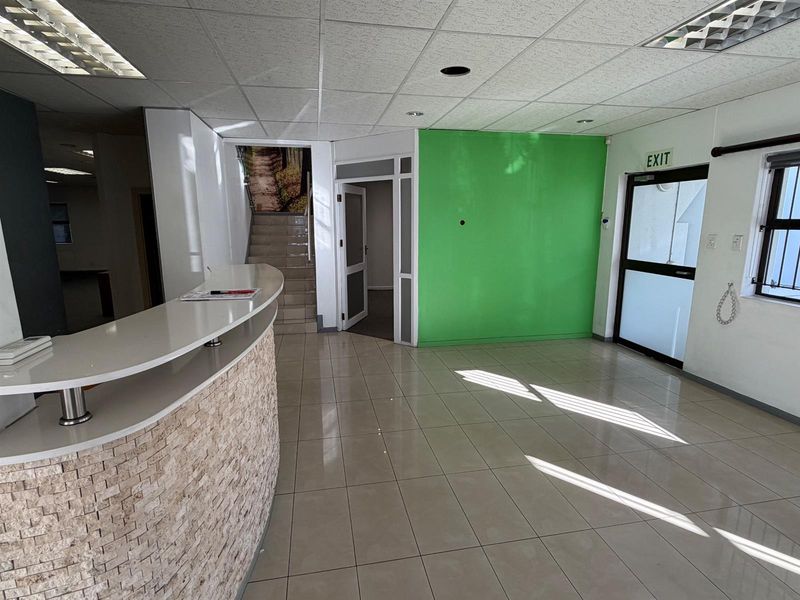 Spacious office entrance area featuring a built-in reception desk, tiled flooring, and a bright, open layout with direct access to stairs and additional office space.